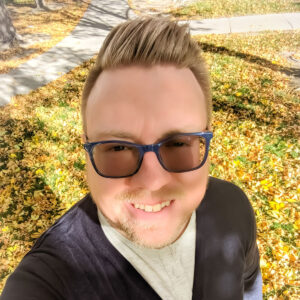 autumn-background Dustin wearing sunglasses, standing in front of autumn leaves in the background